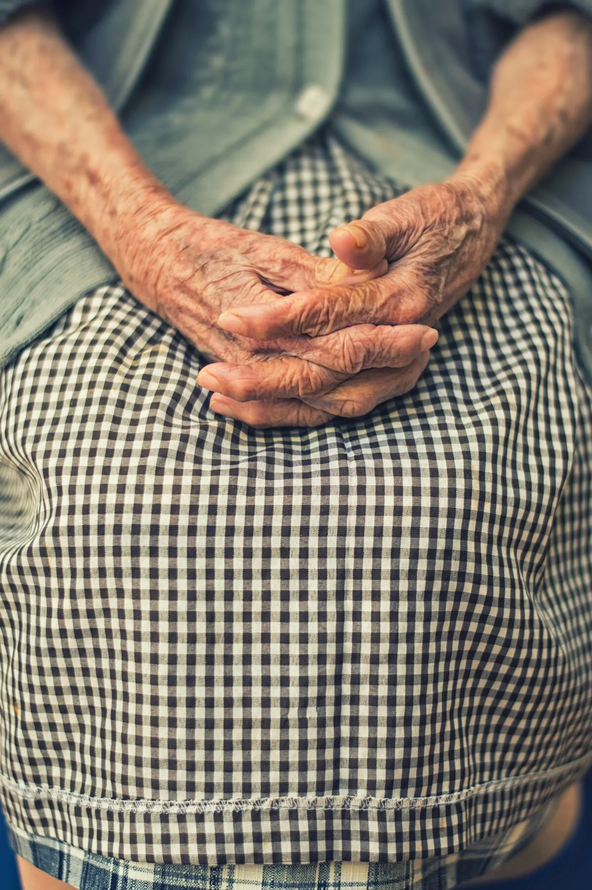 Gevouwen handen van een oudere bewoner op een geruite schort